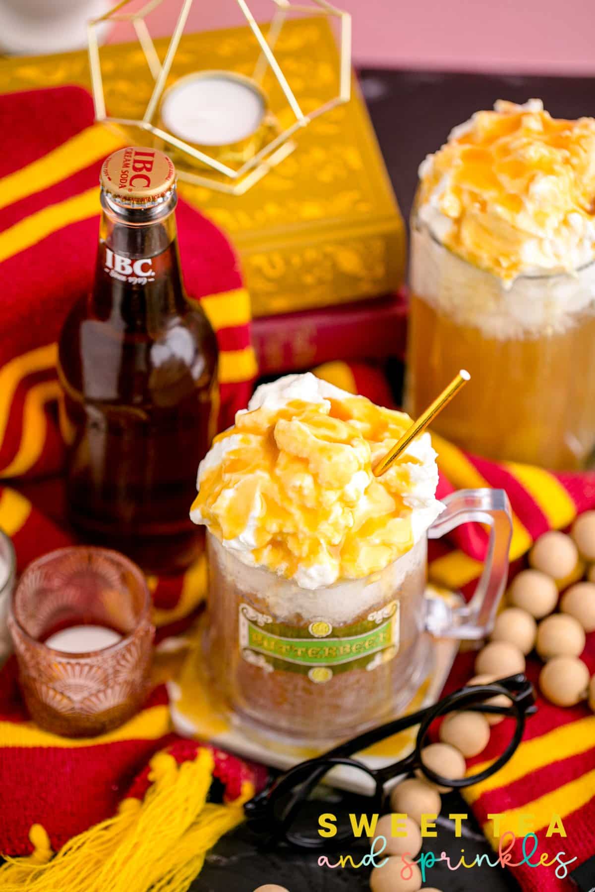 Mug with whipped cream and drizzled butterscotch on top of butterbeer drink with props.