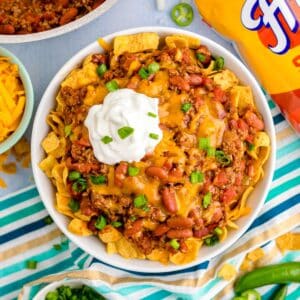 Square image of finished Frito Chili Pie in bowl with toppings.