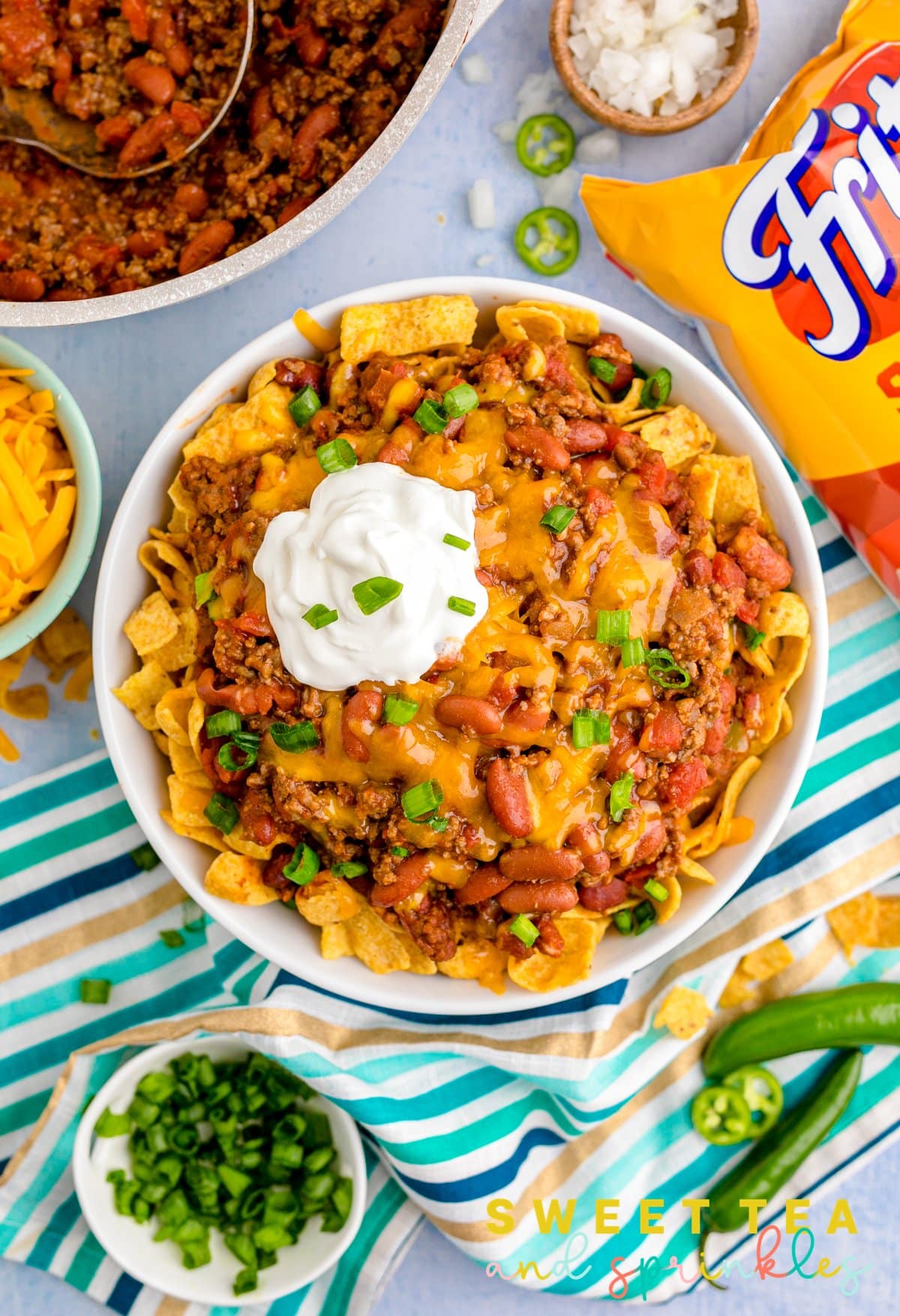 Overhead image of Frito Chili Pie topped with ingredients surrounding bowl.