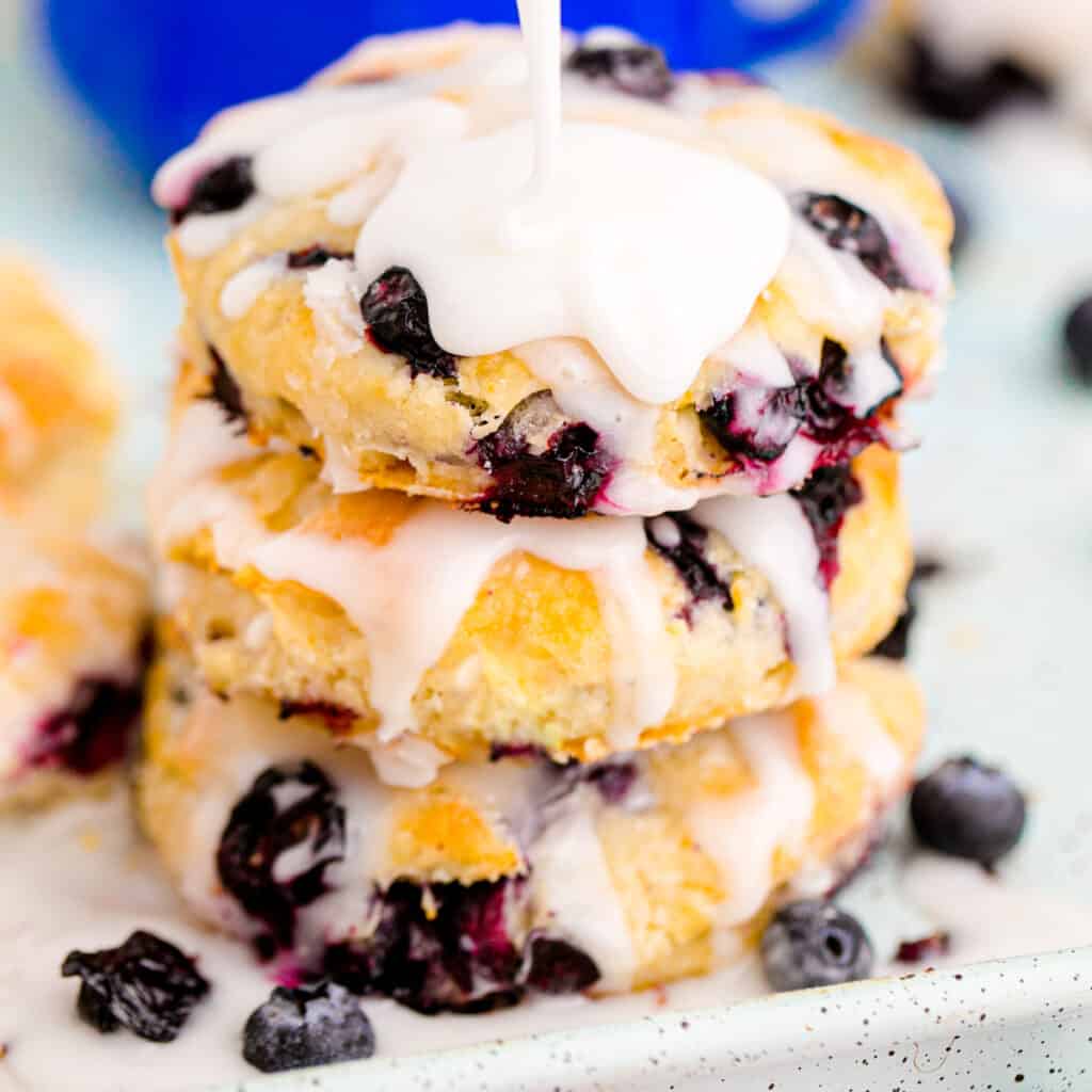 Three biscuits stacked with blueberries baked in and glaze drizzled on top.