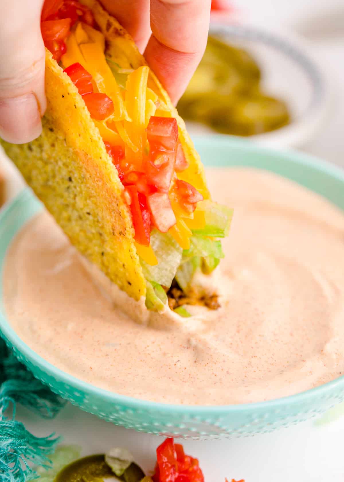 Crispy taco being dipped into a bowl of Taco Bell creamy jalapeno sauce.