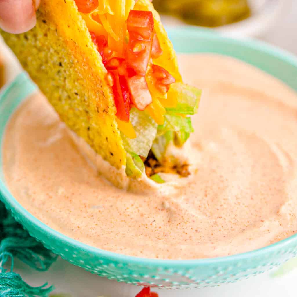 Crispy taco being dipped in a bowl of creamy jalapeno sauce.