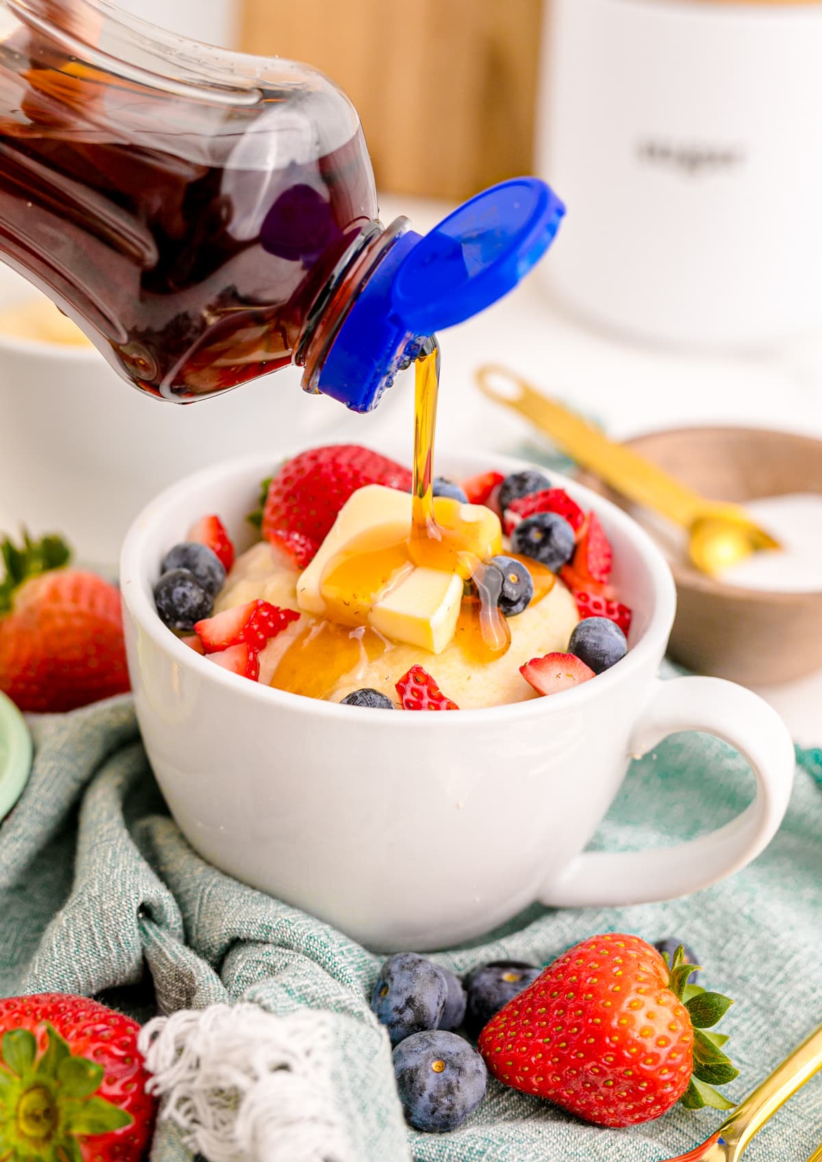 Pancake in a mug with berries, butter and syrup being drizzled over top.