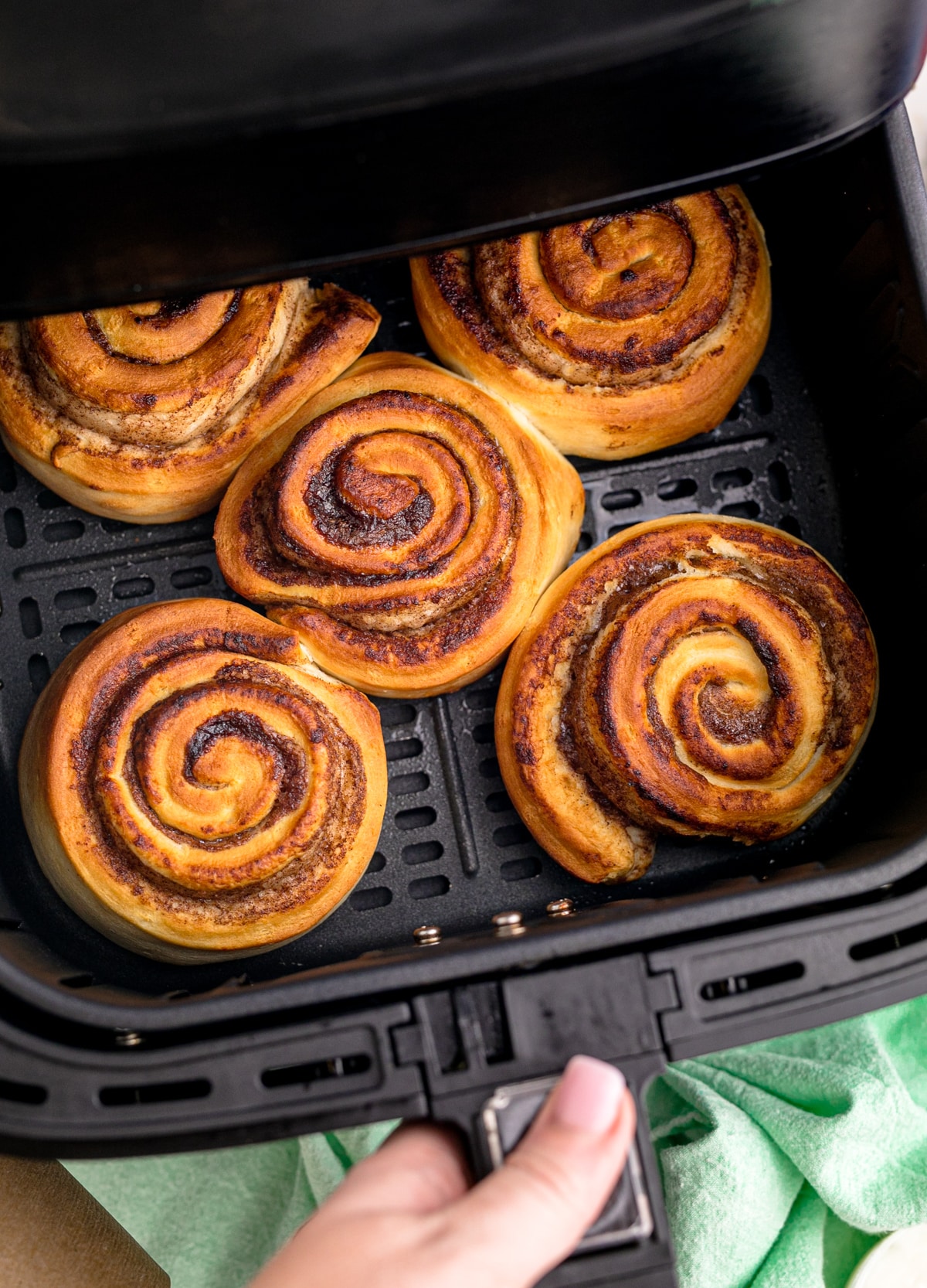 Air fryer being opened with a view of the cooked cinnamon rolls in the basket from above.