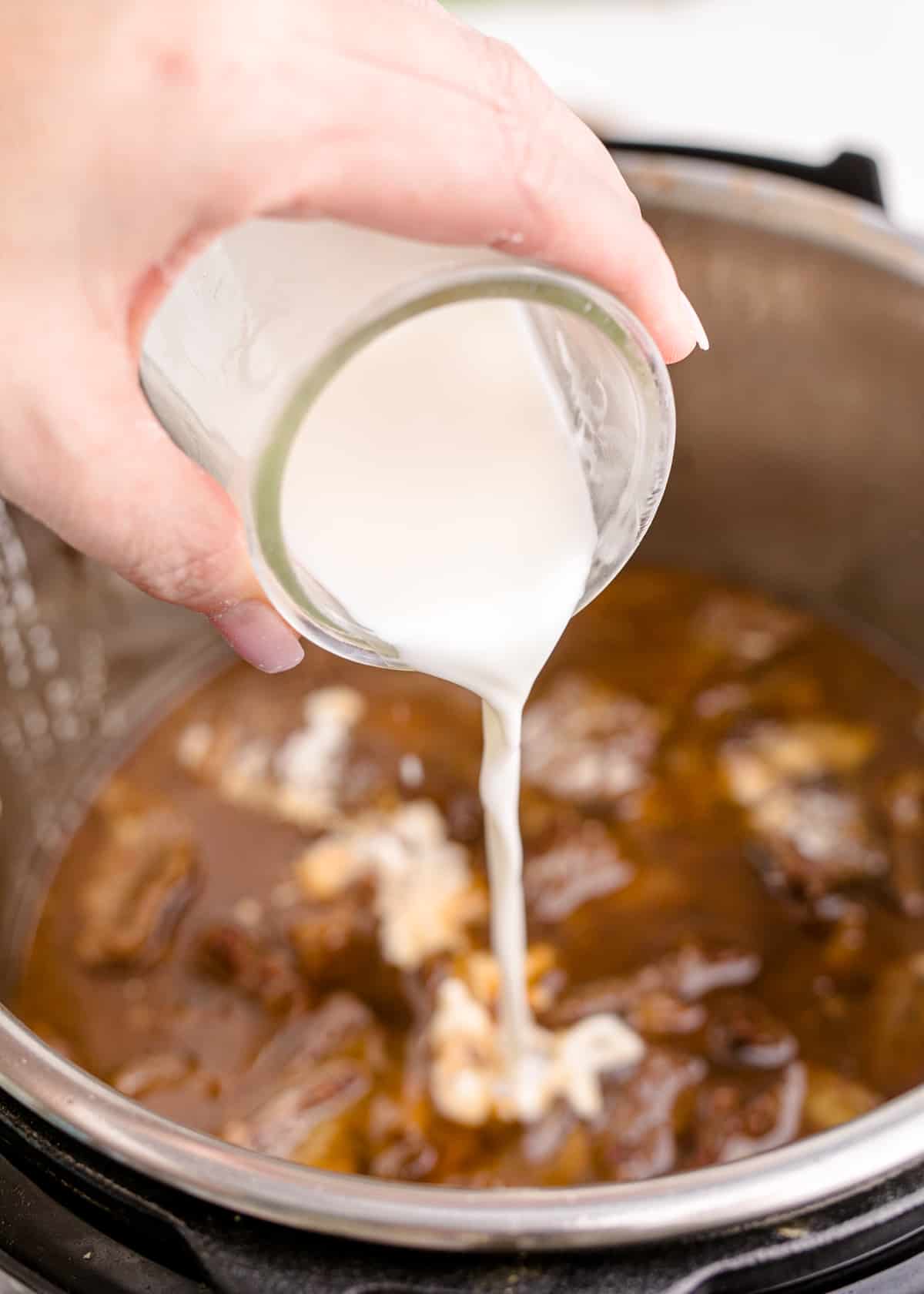 Cornstarch slurry being poured into an Instant Pot overtop of meat and sauces.