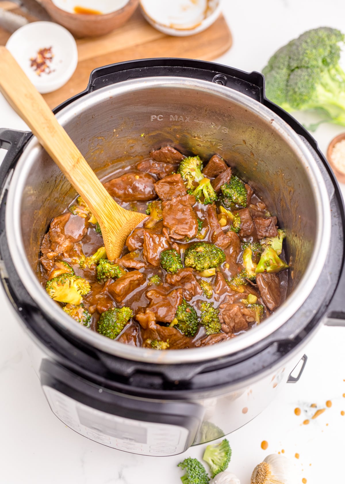 Cooked beef and broccoli in an Instant Pot with a wooden spoon stirring contents inside.