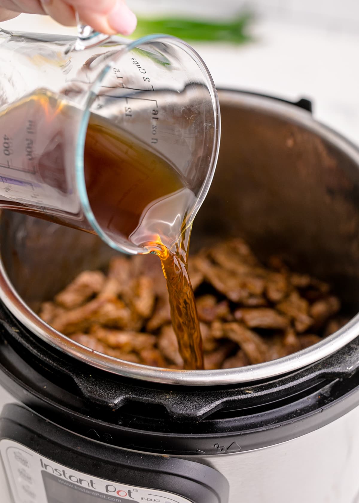 Beef broth being poured into an instant pot over cooked meat.
