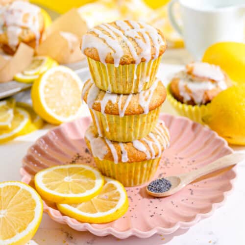 Three poppyseed muffins stacked on top of a pink plate with lemon slices.