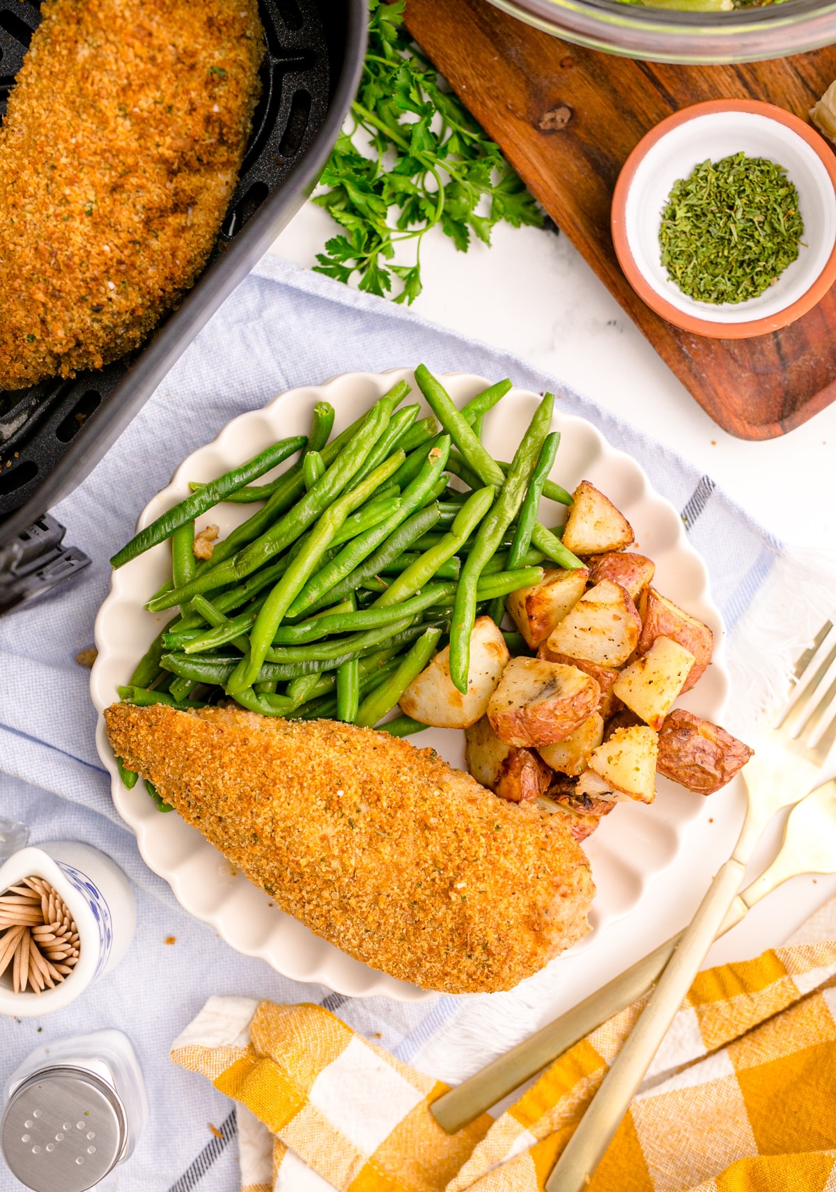 Baked chicken on a plate with roasted potatoes and green beans taken from a bird's eye view.