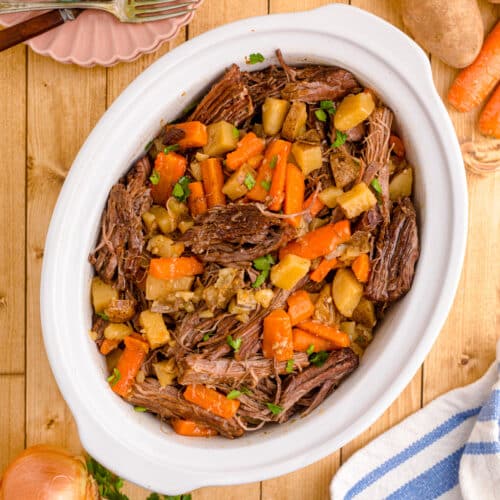 Pulled meat in a white crock pot with carrots and potatoes.