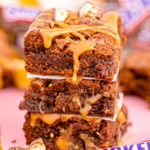 Close up of three layered Snickers bars brownies dripping with caramel.
