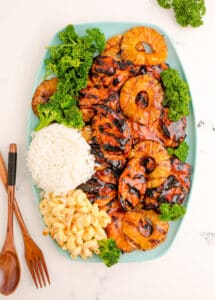 A teal tray with bbq chicken, rice, macaroni salad, and grilled pineapples.
