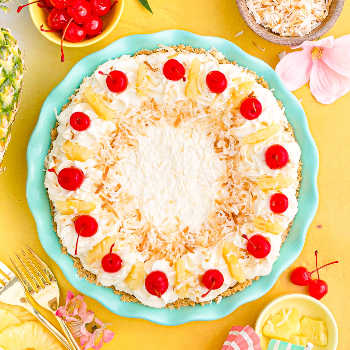 Pina colada pie in a teal pie dish with cherries, toasted coconut and pineapple slices.