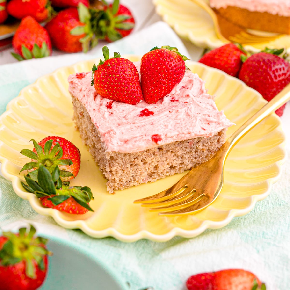 A piece of strawberry sheet cake with strawberry buttercream icing and fresh berries on top.