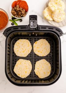 Biscuit dough pizza crusts being baked in an air fryer basket.