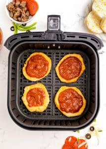 Baked mini pizza crusts topped with marinara sauce in an air fryer basket.