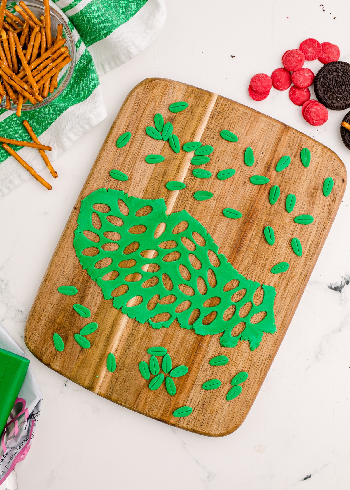 Green leaves cut out of fondant on a cutting board.