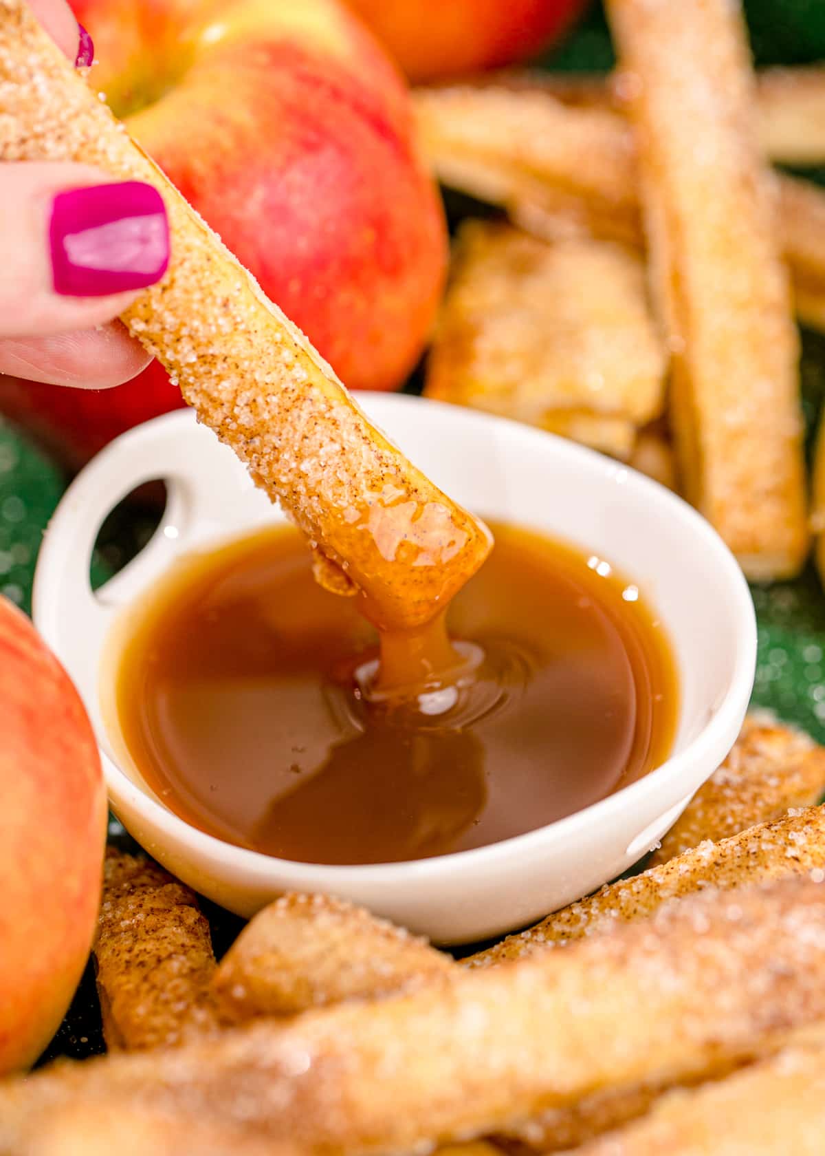 An apple pie fry being dipped into caramel sauce.