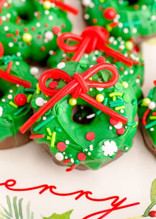 Christmas wreath cookies topped with a red bow and Christmas sprinkles on holiday plate.