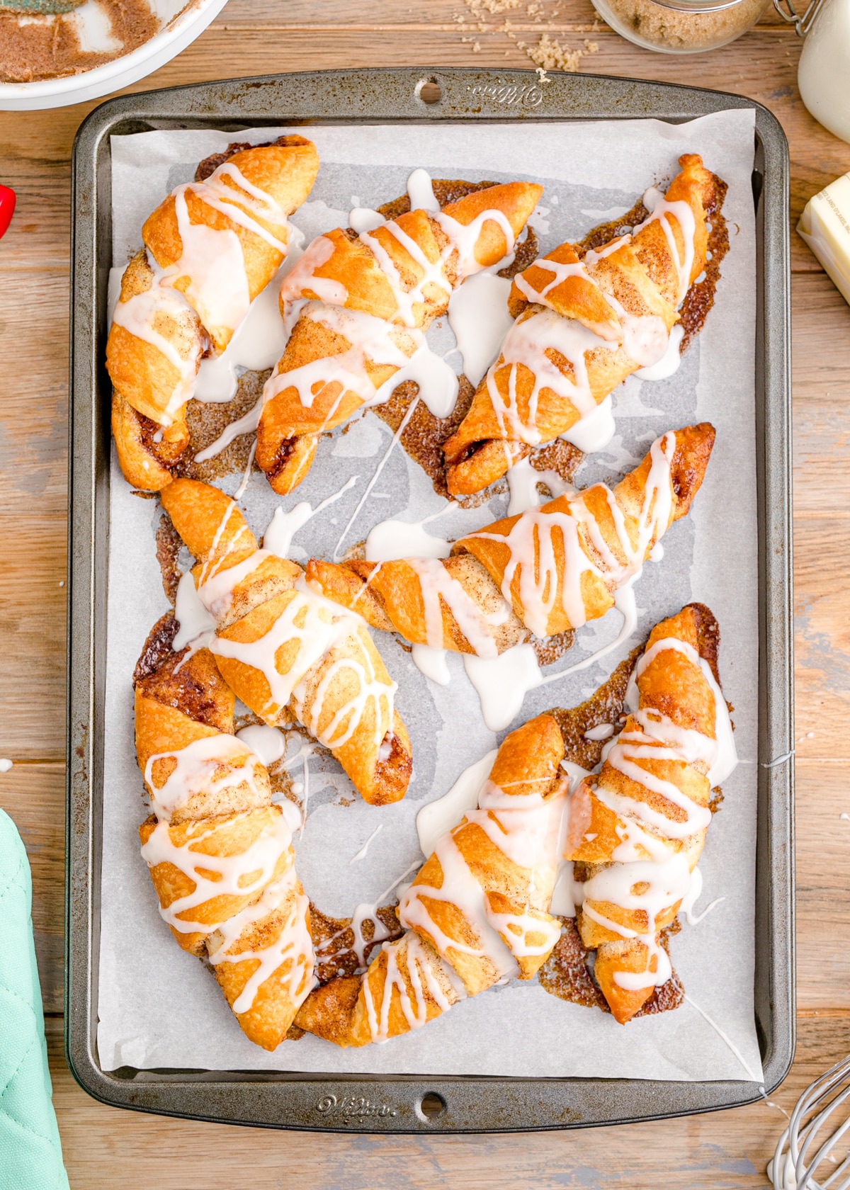 Baked cinnamon crescent rolls drizzled with a powdered sugar icing on a baking sheet.