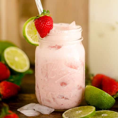 Creamy strawberry limeade poured over ice in a mason jar and served with a lime wedge and one strawberry.