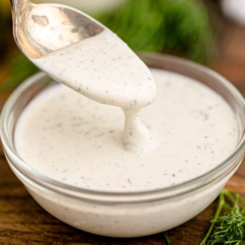 Restaurant style ranch dressing being spooned out of a small glass condiment bowl.