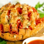 Pull apart pizza bread on a cutting board filled with melted mozzarella cheese and pepperonis.