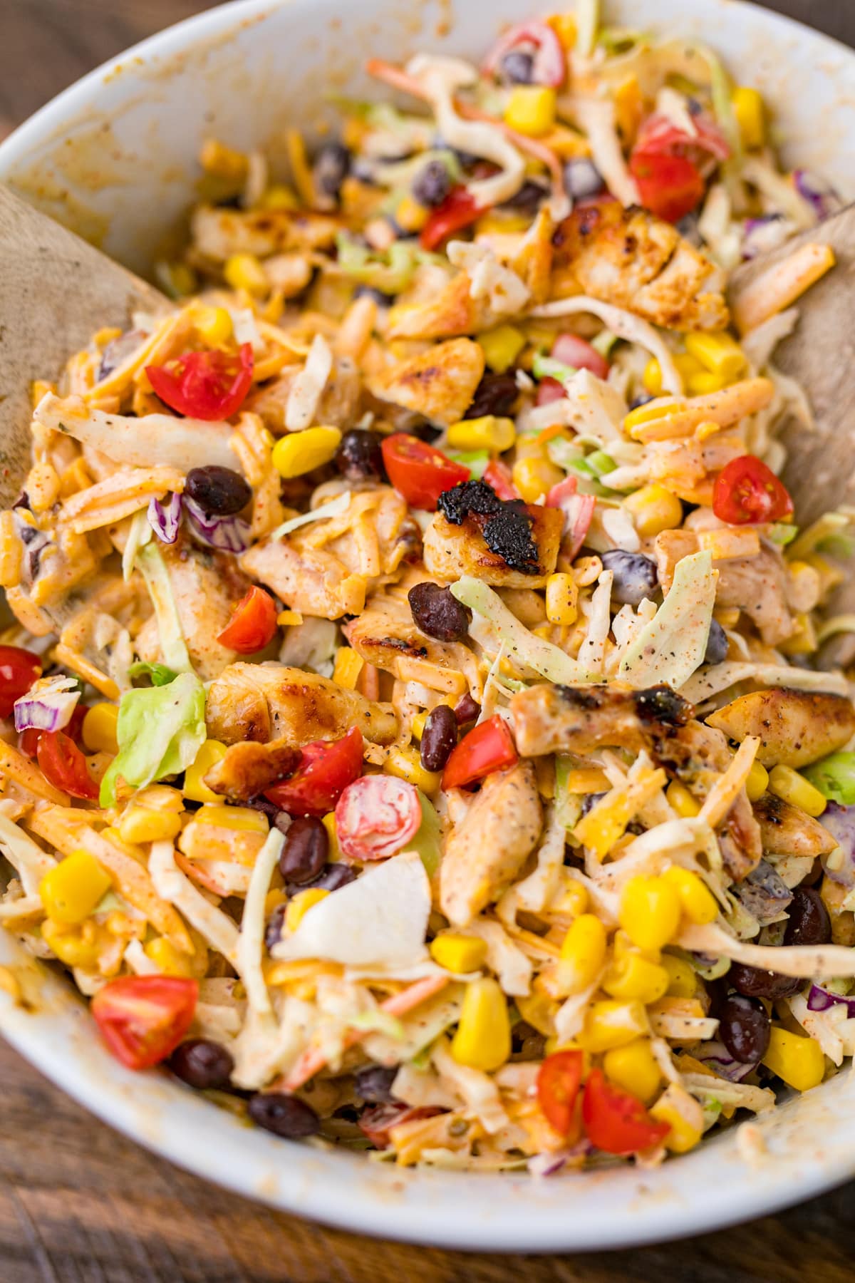 Southwest coleslaw with the chicken, black beans, cheese, southwest dressing, corn and tomatoes in a bowl.