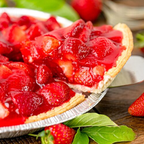 A slice of strawberry pie being taken out of a tin foil pie pan.